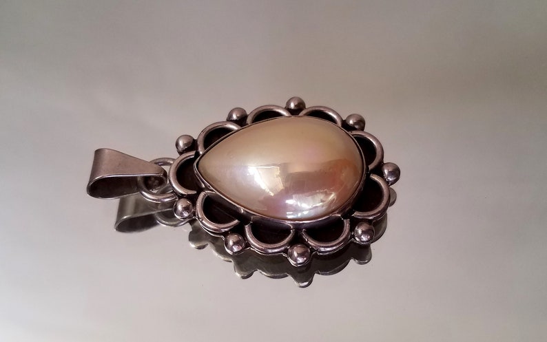 May include: A silver pendant with a large, pearlescent white gemstone set in a decorative, floral-shaped frame.