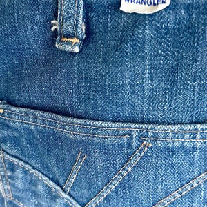 Vintage Wrangler Jeans With Sunburst Stitching and Boot Cut Silhouette. vintage blue jeans. vintage wranglers. vintage sunburst jeans. vintage bell bottoms. vintage wrangler bells. vintage denim bell bottoms. vintage boot cut jeans. vintage boot cut wranglers. vintage boot cut denim. vintage boho jeans. vintage wearer wear. vintage rodeo jeans.