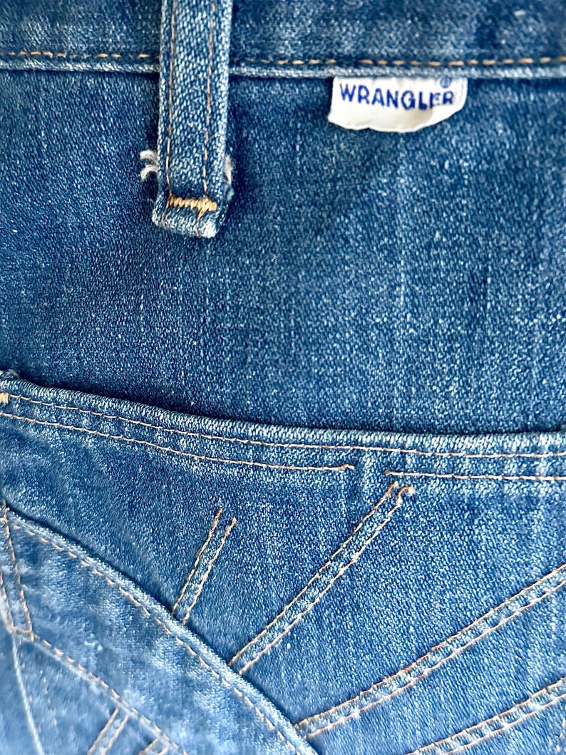 Vintage Wrangler Jeans With Sunburst Stitching and Boot Cut Silhouette. vintage blue jeans. vintage wranglers. vintage sunburst jeans. vintage bell bottoms. vintage wrangler bells. vintage denim bell bottoms. vintage boot cut jeans. vintage boot cut wranglers. vintage boot cut denim. vintage boho jeans. vintage wearer wear. vintage rodeo jeans.