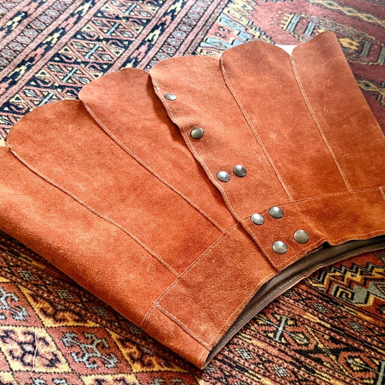 vintage suede skirt in orange rust color with unique scalloped hemline. vintage mini skirt with a series of vertical suede monochrome panels and dark toned brass snaps at front closure. vintage leather skirt. patchwork suede skirt. vintage patchwork skirts. 1960s vintage skirts. vintage 60s skirts. vintage leather patchwork skirt. vintage 1960s mini skirt. vintage suede mini skirts. vintage leather mini skirt. vintage patchwork mini skirt.