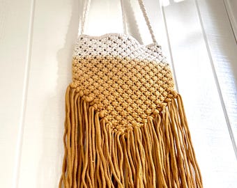 May include: A white and mustard yellow crocheted bag with a long fringe. The bag has a white strap.