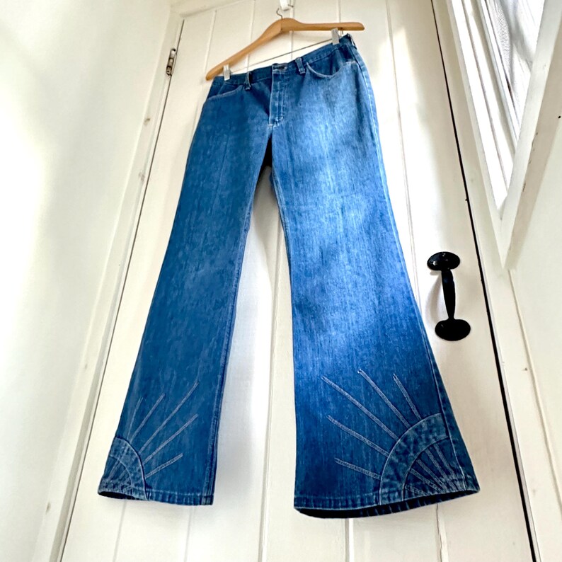 Vintage Wrangler Jeans With Sunburst Stitching and Boot Cut Silhouette. vintage blue jeans. vintage wranglers. vintage sunburst jeans. vintage bell bottoms. vintage wrangler bells. vintage denim bell bottoms. vintage boot cut jeans. vintage boot cut wranglers. vintage boot cut denim. vintage boho jeans. vintage wearer wear. vintage rodeo jeans.