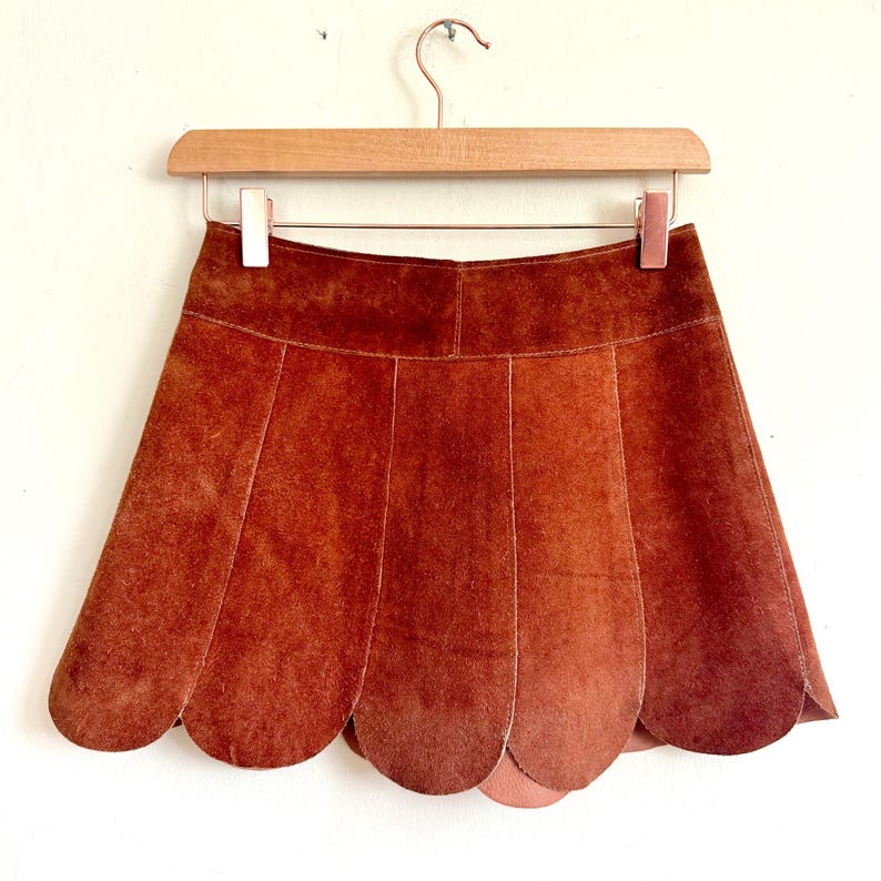 vintage suede skirt in orange rust color with unique scalloped hemline. vintage mini skirt with a series of vertical suede monochrome panels and dark toned brass snaps at front closure. vintage leather skirt. patchwork suede skirt. vintage patchwork skirts. 1960s vintage skirts. vintage 60s skirts. vintage leather patchwork skirt. vintage 1960s mini skirt. vintage suede mini skirts. vintage leather mini skirt. vintage patchwork mini skirt.