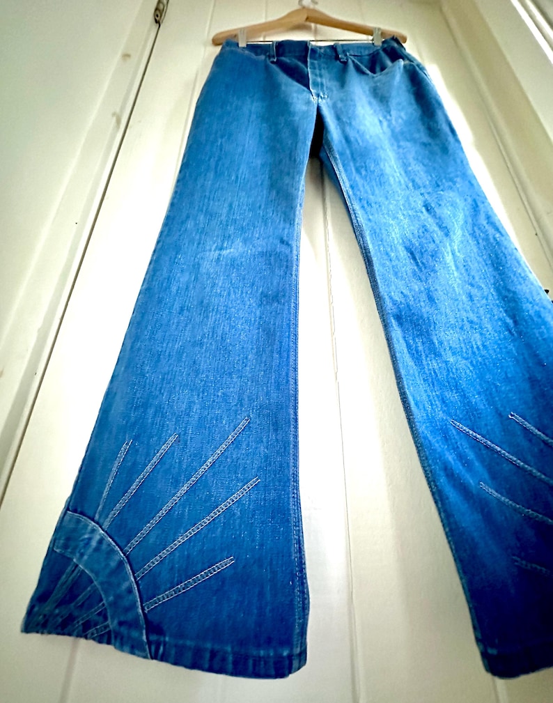 Vintage Wrangler Jeans With Sunburst Stitching and Boot Cut Silhouette. vintage blue jeans. vintage wranglers. vintage sunburst jeans. vintage bell bottoms. vintage wrangler bells. vintage denim bell bottoms. vintage boot cut jeans. vintage boot cut wranglers. vintage boot cut denim. vintage boho jeans. vintage wearer wear. vintage rodeo jeans.