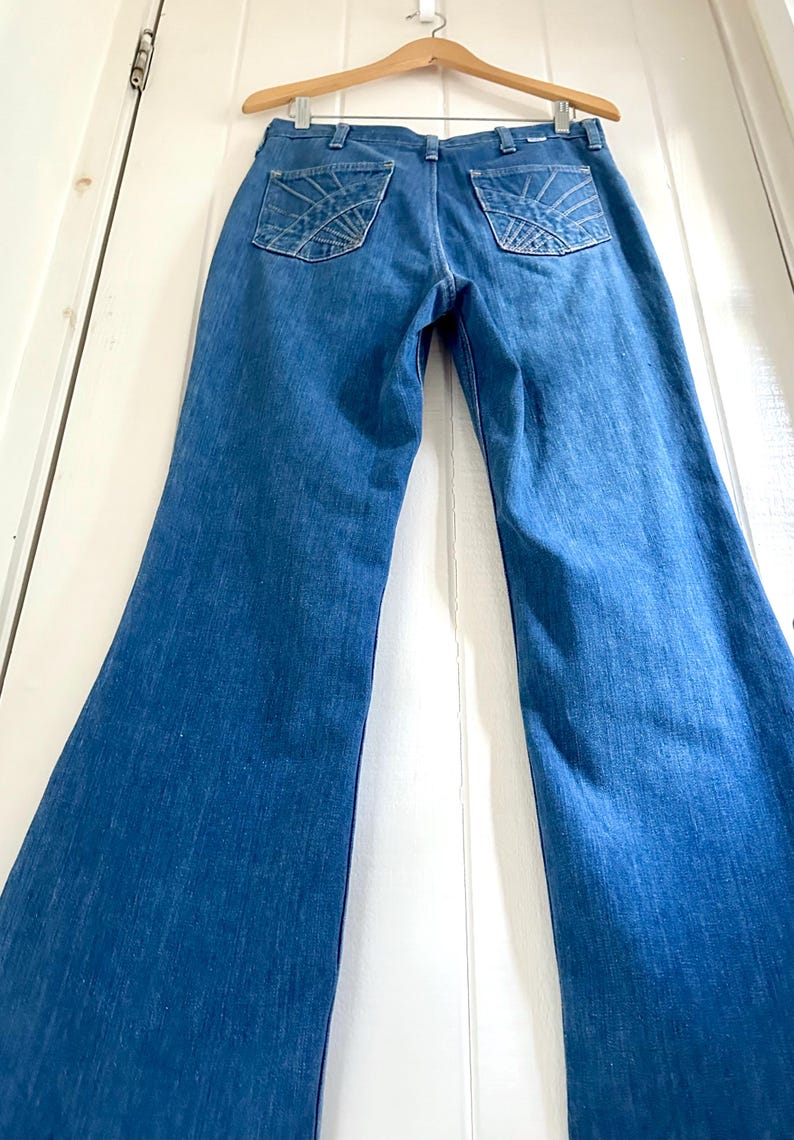 Vintage Wrangler Jeans With Sunburst Stitching and Boot Cut Silhouette. vintage blue jeans. vintage wranglers. vintage sunburst jeans. vintage bell bottoms. vintage wrangler bells. vintage denim bell bottoms. vintage boot cut jeans. vintage boot cut wranglers. vintage boot cut denim. vintage boho jeans. vintage wearer wear. vintage rodeo jeans.