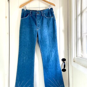 Vintage Wrangler Jeans With Sunburst Stitching and Boot Cut Silhouette. vintage blue jeans. vintage wranglers. vintage sunburst jeans. vintage bell bottoms. vintage wrangler bells. vintage denim bell bottoms. vintage boot cut jeans. vintage boot cut wranglers. vintage boot cut denim. vintage boho jeans. vintage wearer wear. vintage rodeo jeans.