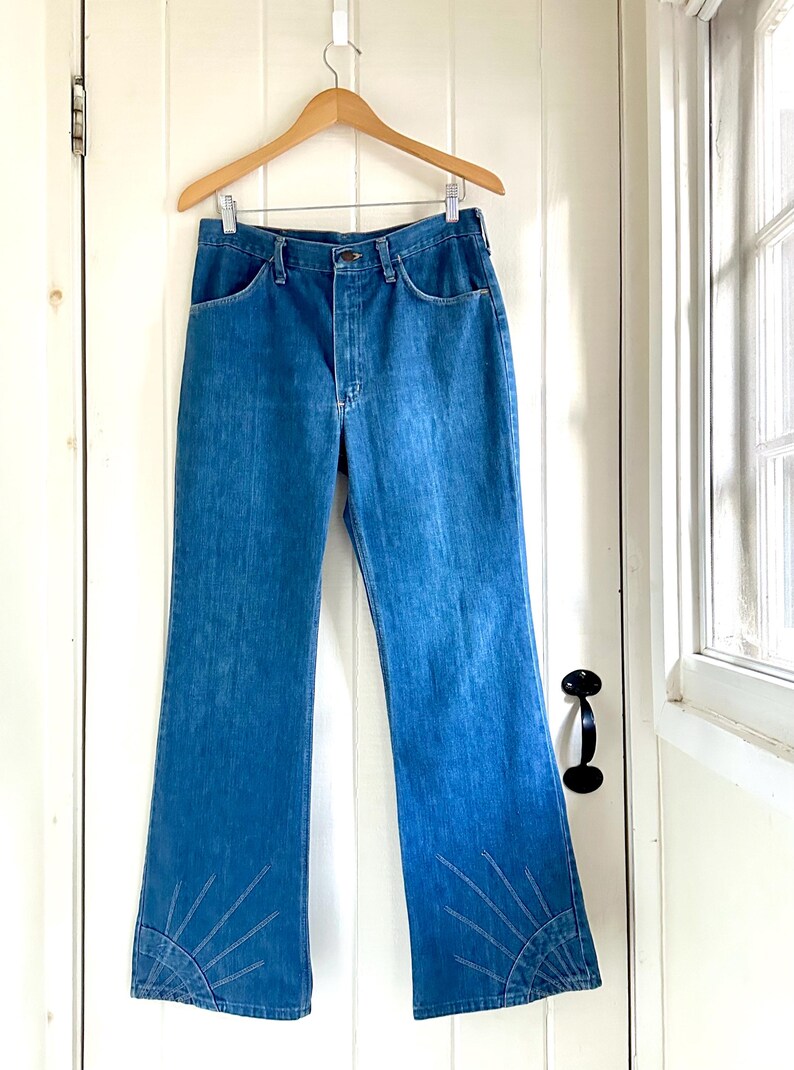 Vintage Wrangler Jeans With Sunburst Stitching and Boot Cut Silhouette. vintage blue jeans. vintage wranglers. vintage sunburst jeans. vintage bell bottoms. vintage wrangler bells. vintage denim bell bottoms. vintage boot cut jeans. vintage boot cut wranglers. vintage boot cut denim. vintage boho jeans. vintage wearer wear. vintage rodeo jeans.