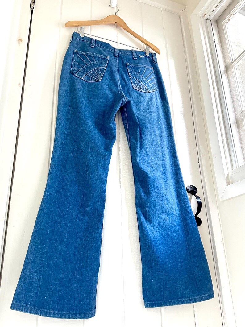 Vintage Wrangler Jeans With Sunburst Stitching and Boot Cut Silhouette. vintage blue jeans. vintage wranglers. vintage sunburst jeans. vintage bell bottoms. vintage wrangler bells. vintage denim bell bottoms. vintage boot cut jeans. vintage boot cut wranglers. vintage boot cut denim. vintage boho jeans. vintage wearer wear. vintage rodeo jeans.