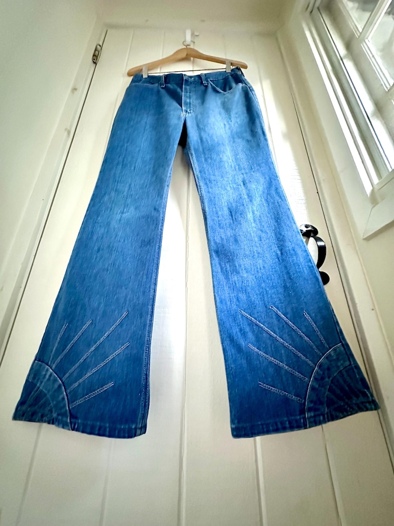 Vintage Wrangler Jeans With Sunburst Stitching and Boot Cut Silhouette. vintage blue jeans. vintage wranglers. vintage sunburst jeans. vintage bell bottoms. vintage wrangler bells. vintage denim bell bottoms. vintage boot cut jeans. vintage boot cut wranglers. vintage boot cut denim. vintage boho jeans. vintage wearer wear. vintage rodeo jeans.