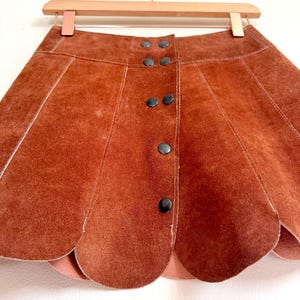 vintage suede skirt in orange rust color with unique scalloped hemline. vintage mini skirt with a series of vertical suede monochrome panels and dark toned brass snaps at front closure. vintage leather skirt. patchwork suede skirt. vintage patchwork skirts. 1960s vintage skirts. vintage 60s skirts. vintage leather patchwork skirt. vintage 1960s mini skirt. vintage suede mini skirts. vintage leather mini skirt. vintage patchwork mini skirt.