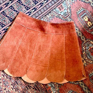 vintage suede skirt in orange rust color with unique scalloped hemline. vintage mini skirt with a series of vertical suede monochrome panels and dark toned brass snaps at front closure. vintage leather skirt. patchwork suede skirt. vintage patchwork skirts. 1960s vintage skirts. vintage 60s skirts. vintage leather patchwork skirt. vintage 1960s mini skirt. vintage suede mini skirts. vintage leather mini skirt. vintage patchwork mini skirt.