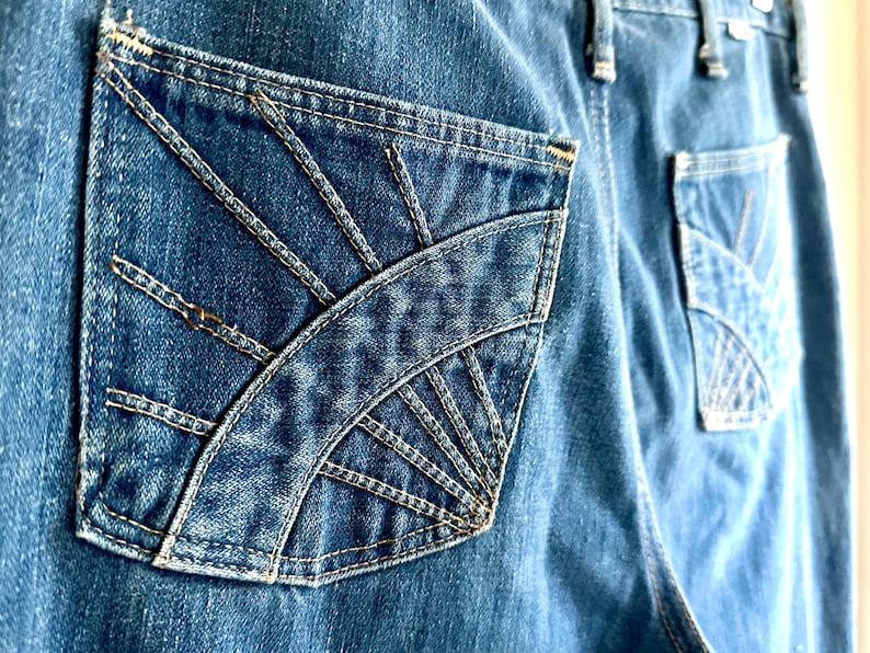 Vintage Wrangler Jeans With Sunburst Stitching and Boot Cut Silhouette. vintage blue jeans. vintage wranglers. vintage sunburst jeans. vintage bell bottoms. vintage wrangler bells. vintage denim bell bottoms. vintage boot cut jeans. vintage boot cut wranglers. vintage boot cut denim. vintage boho jeans. vintage wearer wear. vintage rodeo jeans.