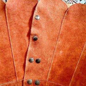 vintage suede skirt in orange rust color with unique scalloped hemline. vintage mini skirt with a series of vertical suede monochrome panels and dark toned brass snaps at front closure. vintage leather skirt. patchwork suede skirt. vintage patchwork skirts. 1960s vintage skirts. vintage 60s skirts. vintage leather patchwork skirt. vintage 1960s mini skirt. vintage suede mini skirts. vintage leather mini skirt. vintage patchwork mini skirt.