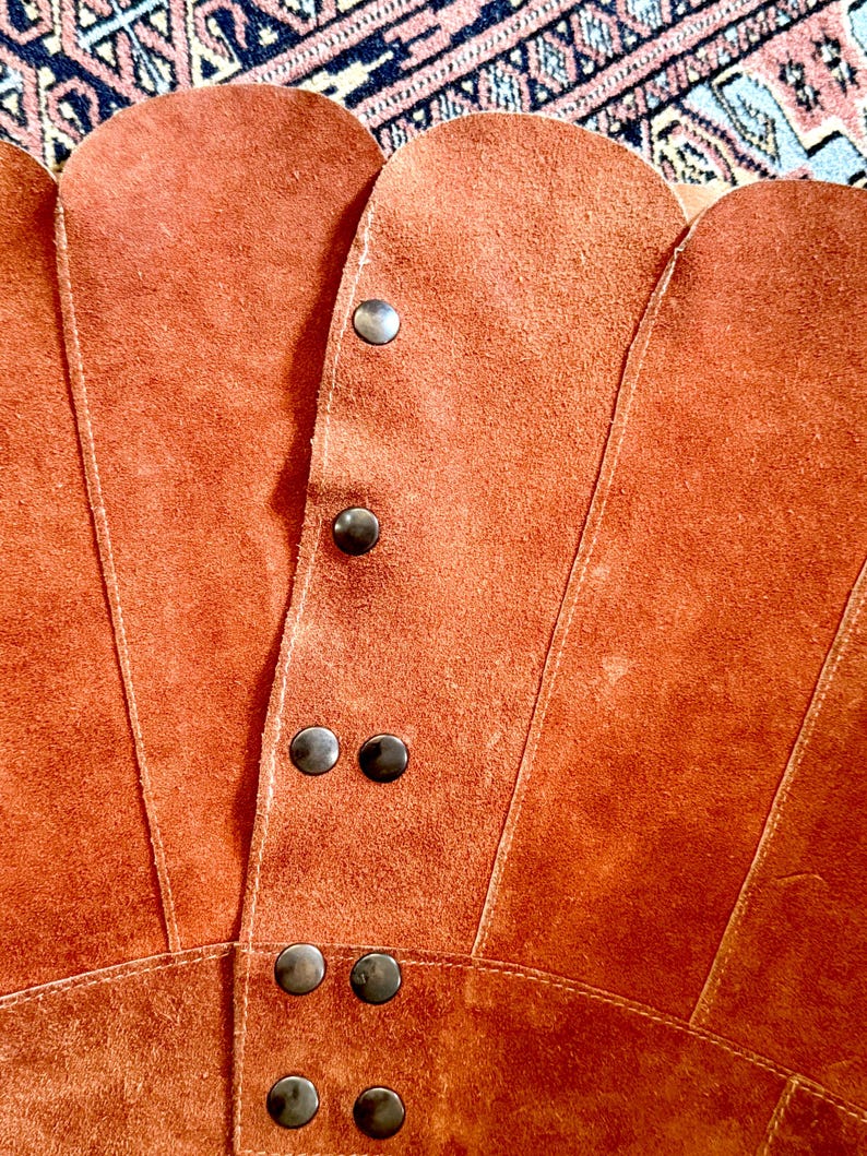 vintage suede skirt in orange rust color with unique scalloped hemline. vintage mini skirt with a series of vertical suede monochrome panels and dark toned brass snaps at front closure. vintage leather skirt. patchwork suede skirt. vintage patchwork skirts. 1960s vintage skirts. vintage 60s skirts. vintage leather patchwork skirt. vintage 1960s mini skirt. vintage suede mini skirts. vintage leather mini skirt. vintage patchwork mini skirt.