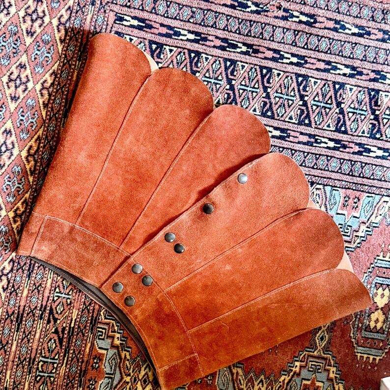 vintage suede skirt in orange rust color with unique scalloped hemline. vintage mini skirt with a series of vertical suede monochrome panels and dark toned brass snaps at front closure. vintage leather skirt. patchwork suede skirt. vintage patchwork skirts. 1960s vintage skirts. vintage 60s skirts. vintage leather patchwork skirt. vintage 1960s mini skirt. vintage suede mini skirts. vintage leather mini skirt. vintage patchwork mini skirt.