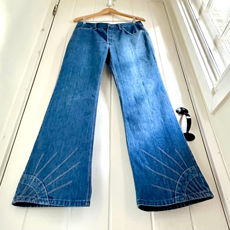 Vintage Wrangler Jeans With Sunburst Stitching and Boot Cut Silhouette. vintage blue jeans. vintage wranglers. vintage sunburst jeans. vintage bell bottoms. vintage wrangler bells. vintage denim bell bottoms. vintage boot cut jeans. vintage boot cut wranglers. vintage boot cut denim. vintage boho jeans. vintage wearer wear. vintage rodeo jeans.