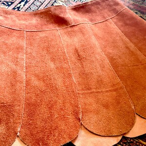 vintage suede skirt in orange rust color with unique scalloped hemline. vintage mini skirt with a series of vertical suede monochrome panels and dark toned brass snaps at front closure. vintage leather skirt. patchwork suede skirt. vintage patchwork skirts. 1960s vintage skirts. vintage 60s skirts. vintage leather patchwork skirt. vintage 1960s mini skirt. vintage suede mini skirts. vintage leather mini skirt. vintage patchwork mini skirt.