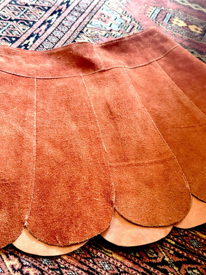 vintage suede skirt in orange rust color with unique scalloped hemline. vintage mini skirt with a series of vertical suede monochrome panels and dark toned brass snaps at front closure. vintage leather skirt. patchwork suede skirt. vintage patchwork skirts. 1960s vintage skirts. vintage 60s skirts. vintage leather patchwork skirt. vintage 1960s mini skirt. vintage suede mini skirts. vintage leather mini skirt. vintage patchwork mini skirt.