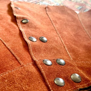 vintage suede skirt in orange rust color with unique scalloped hemline. vintage mini skirt with a series of vertical suede monochrome panels and dark toned brass snaps at front closure. vintage leather skirt. patchwork suede skirt. vintage patchwork skirts. 1960s vintage skirts. vintage 60s skirts. vintage leather patchwork skirt. vintage 1960s mini skirt. vintage suede mini skirts. vintage leather mini skirt. vintage patchwork mini skirt.