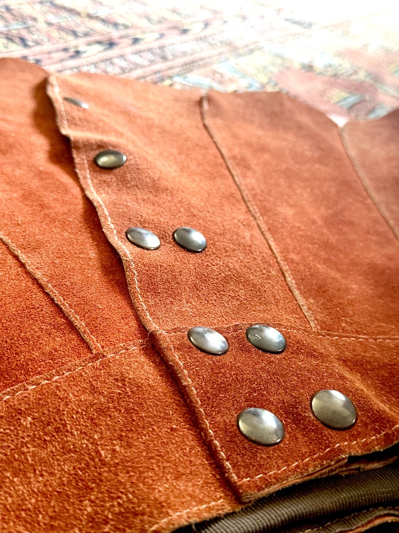 vintage suede skirt in orange rust color with unique scalloped hemline. vintage mini skirt with a series of vertical suede monochrome panels and dark toned brass snaps at front closure. vintage leather skirt. patchwork suede skirt. vintage patchwork skirts. 1960s vintage skirts. vintage 60s skirts. vintage leather patchwork skirt. vintage 1960s mini skirt. vintage suede mini skirts. vintage leather mini skirt. vintage patchwork mini skirt.