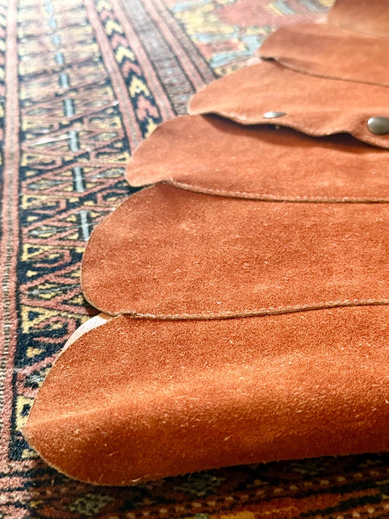 vintage suede skirt in orange rust color with unique scalloped hemline. vintage mini skirt with a series of vertical suede monochrome panels and dark toned brass snaps at front closure. vintage leather skirt. patchwork suede skirt. vintage patchwork skirts. 1960s vintage skirts. vintage 60s skirts. vintage leather patchwork skirt. vintage 1960s mini skirt. vintage suede mini skirts. vintage leather mini skirt. vintage patchwork mini skirt.