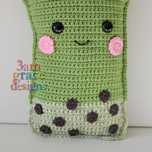 Puede incluir: Juguete de peluche de crochet verde con forma de taza de boba con una pajita de crochet blanco. El juguete tiene una cara sonriente con ojos negros y mejillas rosadas. La parte inferior de la taza está decorada con perlas de boba de crochet marrón.