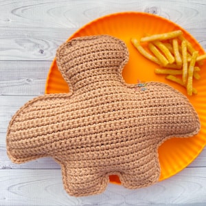 May include: A crocheted brown dinosaur toy on an orange plate with french fries.
