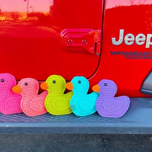 Peut inclure: Cinq canards en crochet align&eacute;s en rang. Les canards sont rose, corail, vert, bleu et violet.