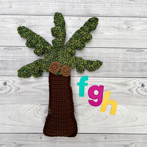 Puede incluir: Un palmera de crochet marrón con hojas verdes y dos adornos marrones en forma de coco. Las letras f, g y h están en el fondo.