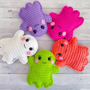 May include: Five colorful, handmade crochet plush toys in the shape of friendly ghosts and monsters. The toys are in shades of white, purple, pink, orange, and green. Each has black eyes and pink cheeks, with a smiling mouth.
