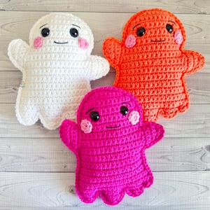May include: Three handmade crochet ghost dolls in white, orange, and pink. Each ghost has black eyes, a smiling mouth, and pink blush. The dolls are soft and plush, perfect for Halloween or as a cute decorative item.