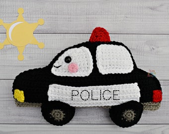 May include: A black and white crocheted police car toy with a red light on top. The car has a smiling face with black eyes and pink cheeks. The word "POLICE" is stitched in black on the side of the car.