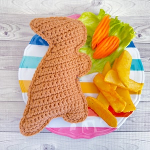 May include: A brown crocheted dinosaur toy on a colorful striped plate with potato wedges and a green salad with carrot slices.