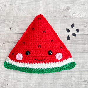 May include: A crocheted watermelon plush toy with a smiling face, black eyes, and pink cheeks. The watermelon is red with a white and green rind. There are black watermelon seeds scattered around the toy.