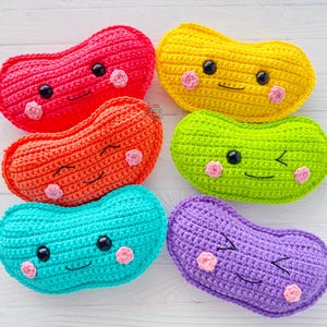 May include: Five crocheted bean-shaped plush toys with smiling faces. The bean-shaped toys are in the colours red, orange, yellow, green, and purple.
