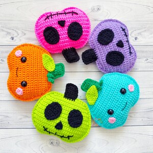 Op de afbeelding: Vijf gehaakte Halloween-thema pompoenen. E&eacute;n is oranje met een schattig gezicht, &eacute;&eacute;n is roze met een schedelgezicht, &eacute;&eacute;n is paars met een schedelgezicht, &eacute;&eacute;n is groen met een schedelgezicht en &eacute;&eacute;n is blauw met een schattig gezicht.