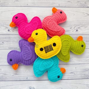 Peut inclure: Un groupe de six jouets en crochet en forme de canard de diff&eacute;rentes couleurs, dont le rose, le violet, le jaune, le vert et le bleu. Les canards sont dispos&eacute;s en cercle sur une surface en bois blanc.