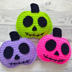 Op de afbeelding: Drie gehaakte Halloween-pompoenen met zwarte ogen en gestikte monden. E&eacute;n pompoen is groen, &eacute;&eacute;n is paars en &eacute;&eacute;n is roze.