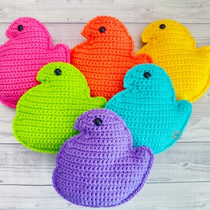 May include: Six crocheted plush toys shaped like Peeps, a popular marshmallow candy. The toys are in various colors: pink, orange, yellow, green, blue, and purple.