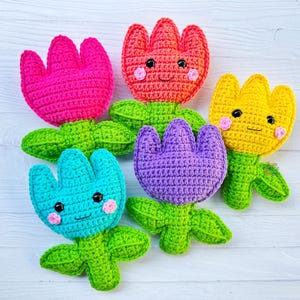 May include: Five colourful, handmade crochet flower toys. The flowers are pink, red, yellow, purple, and turquoise, each with a smiling face, green leaves, and a stem. These soft toys are ideal for children.