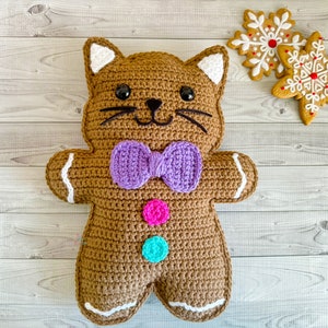 May include: A crocheted gingerbread cat toy with a purple bow, white icing details, and colorful buttons.