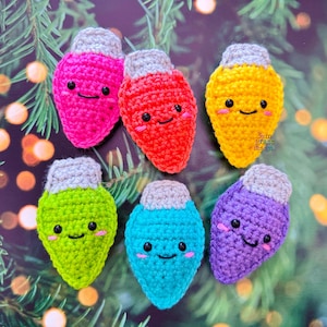May include: A collection of seven colorful, crocheted Christmas light ornaments. Each light is a different color: pink, red, yellow, green, blue, and purple. They have gray tops and smiling faces. The background is a blurred image of Christmas tree branches.