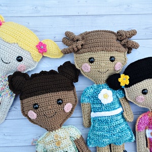 May include: Four crocheted dolls with different hair colors and outfits. The dolls are wearing colorful dresses and have smiling faces with black eyes and pink cheeks.