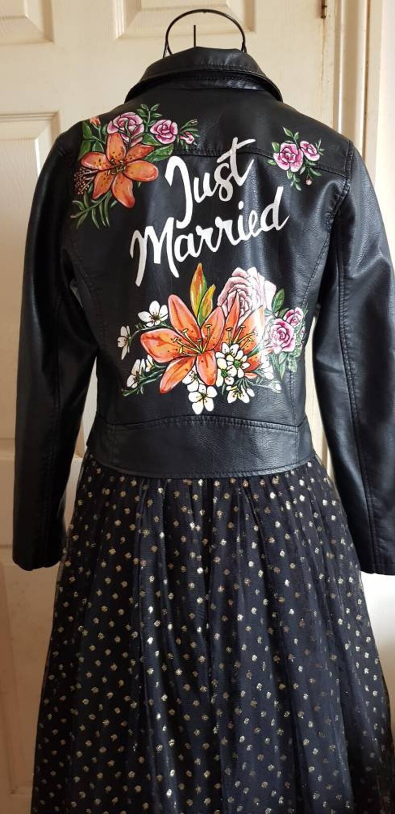 May include: A black leather jacket with a floral design and the words "Just Married" painted on the back. The jacket is paired with a black tulle skirt with gold polka dots.