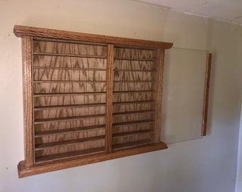 May include: A wooden display case with multiple shelves and a sliding glass door. The case is made of light brown wood and is mounted on a wall. The shelves are designed to hold small items.
