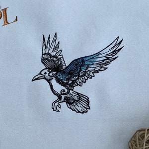 May include: White fabric placemat with a blue and black embroidered design of a bird in flight. The placemat has the initials "C&L" embroidered in the top left corner.