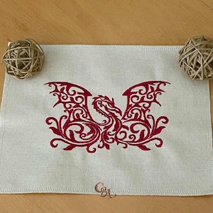 May include: A white linen tea towel with a red embroidered design of a stylized dragon with intricate details.