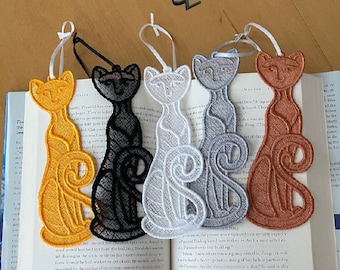 May include: Five embroidered cat bookmarks in different colors: yellow, black, white, gray, and orange. The bookmarks are all in the shape of a cat with a curled tail.