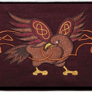 Può includere: Toppa ricamata con un uccello marrone con le ali spiegate, circondato da intricati nodi celtici dorati su uno sfondo bordeaux.