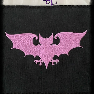 May include: Black fabric with a detailed pink bat embroidery. The bat design features intricate patterns and a stylized appearance. The letters "C&L" are in the upper corner. The overall aesthetic is gothic.
